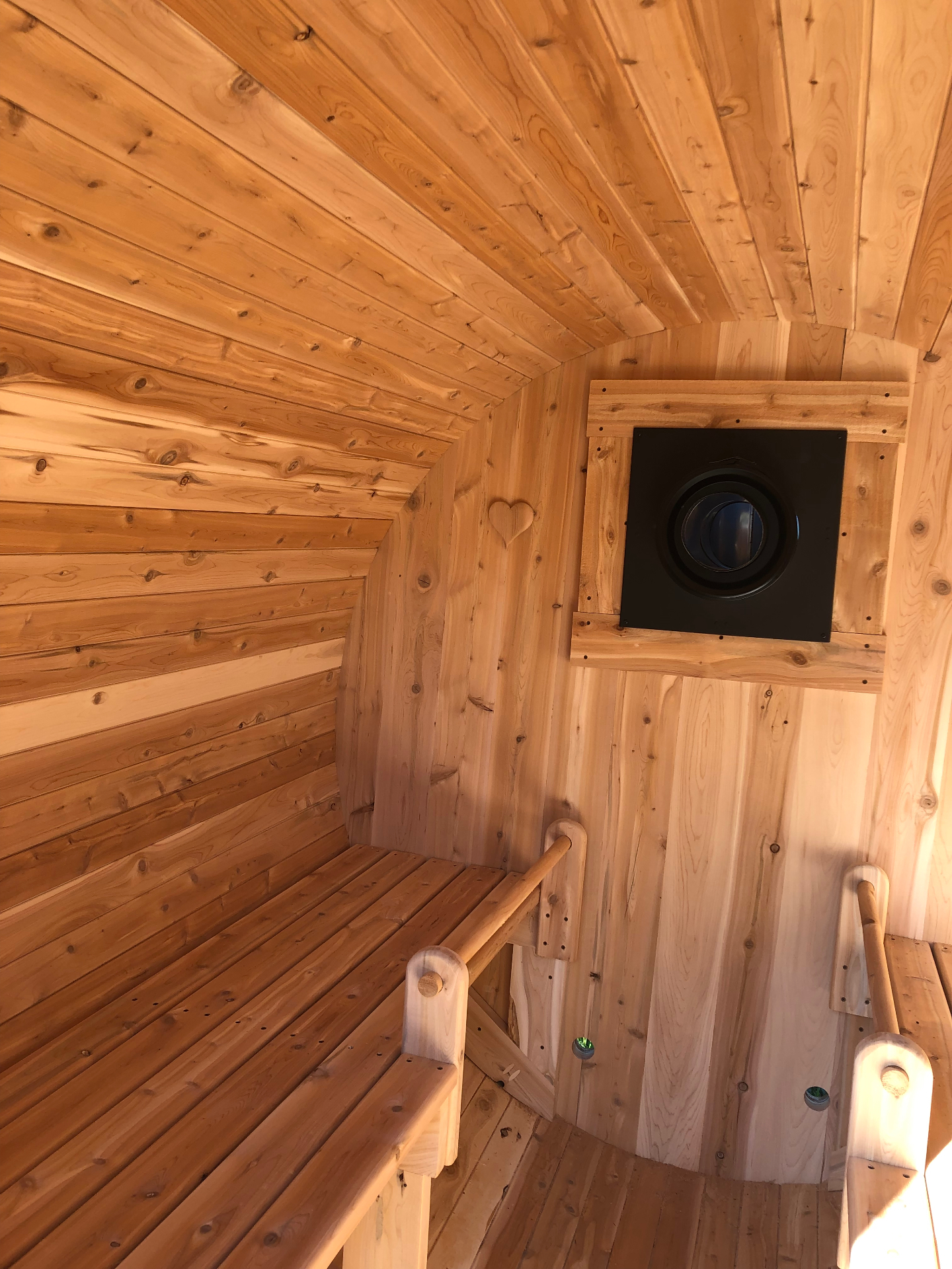 Intérieur d'un sauna baril du Québec en cèdre blanc avec hublot carré noir et cœur sculpté