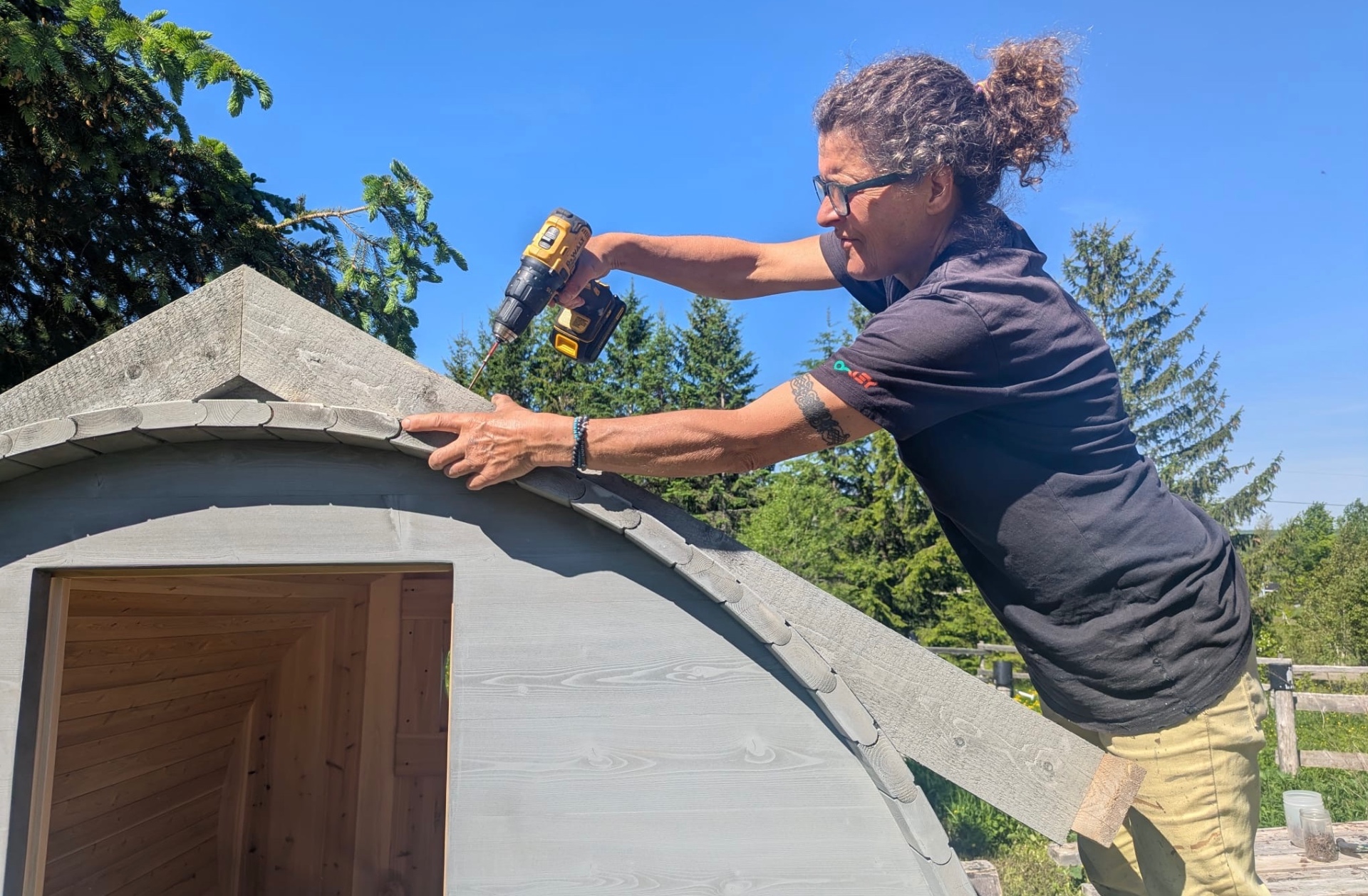 Artisane vissant les bardeaux de cèdre sur le toit d'un sauna baril du Québec
