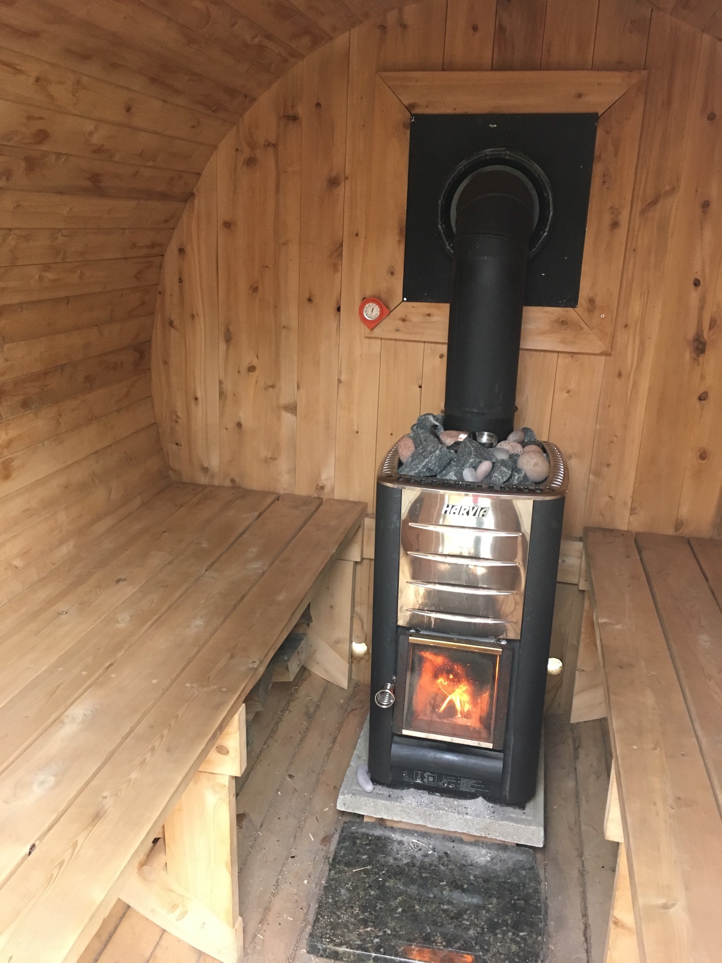 Poêle à bois Harvia allumé avec pierres chaudes dans un sauna baril du Québec en cèdre blanc