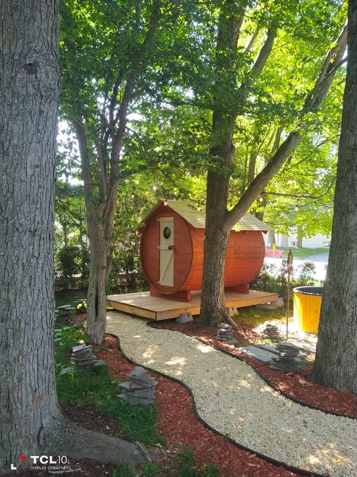 Sauna baril du Québec rouge en cèdre blanc sur terrasse en bois entre les arbres