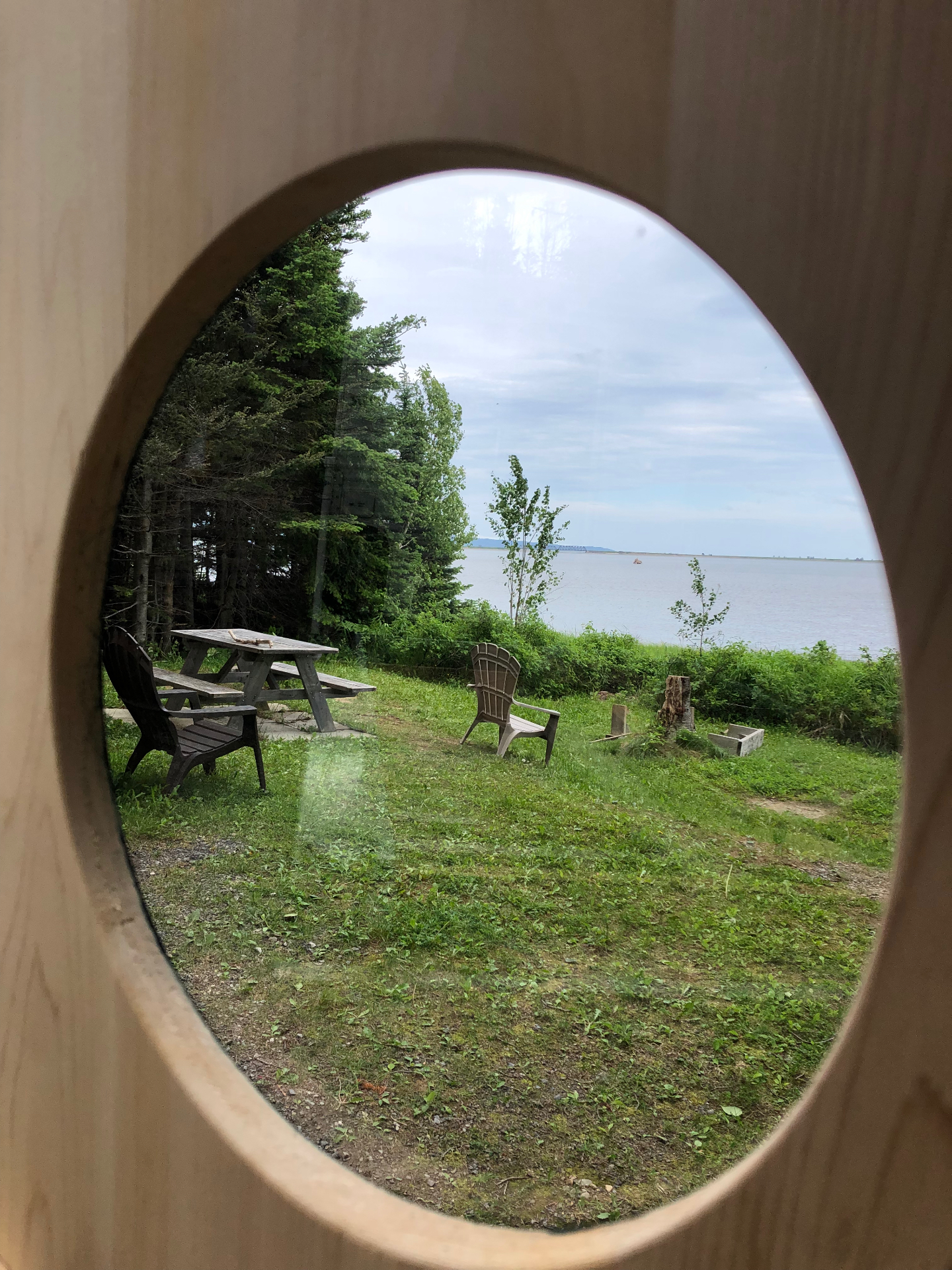 Vue sur le fleuve à travers le hublot ovale d'un sauna baril du Québec en cèdre blanc